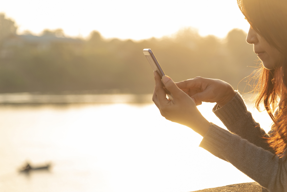 Woman holding mobile phone outdoors surfing the internet.